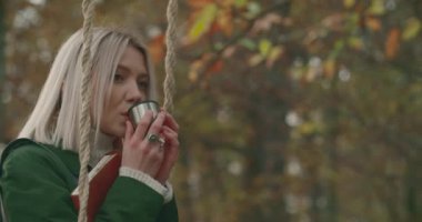 Sonbaharda soğuk bir parkın ortasında sıcak çay içerken sallanan bir kadın. Genç kadın hayatı, hafızayı hatırlatıyor. Ağır çekim..