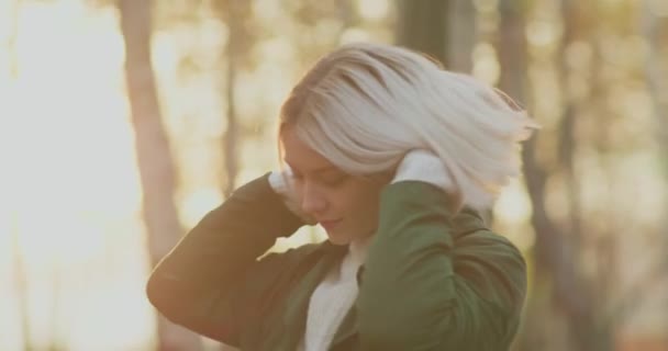 Beautiful woman plays with her blonde hair in a park in an autumn day sunlight surprise her. slow motion — Stock Video