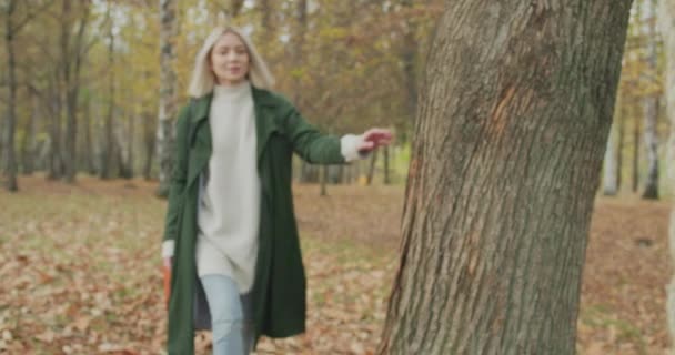 若いブロンドの女性は秋に葉の上を歩くロープスイングに達する。ロープのスイングに歩いて女性。美しい女性の公園では、フロントビュースイング。スローモーション — ストック動画