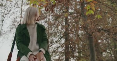 Genç bir kadın, sonbahar günbatımında büyük bir ağacın altında, ufka bakıyor. Yavaş çekim.