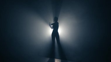 Formda bir kadın antrenmanın sonunda esneme hareketleri yapar. Sportif kadın siluetinin arka ışığı. Düşük hareket.
