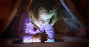Çocuk sarışın, beyaz, dijital boyalı, gece battaniyesinin altında tablet uygulaması olan bir kız. Modern teknoloji çocukluk çocuğu evde kullanıyor. 4k video