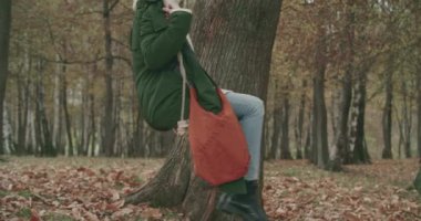 Sonbaharda yaşlı bir ağacın altında sallanan genç bir kadının yan görüntüsü. yavaş çekim