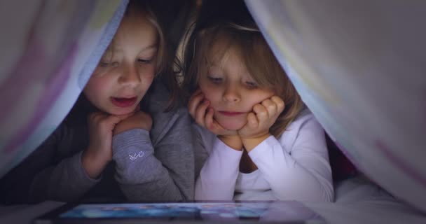 Kind blond Kaukasisch meisje met vriend of zus kijken film of animatie op tablet app onder bed deken 's nachts. Moderne technologie die kinderen thuis gebruiken. 4k video — Stockvideo