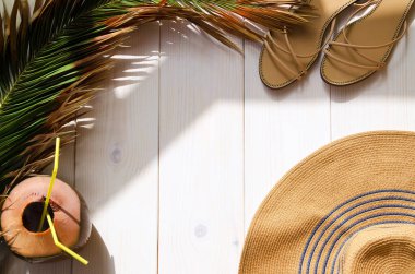 Tropik palmiye yaprağı, güneş şapkası, hindistan cevizi kokteyli ve beyaz ahşap arka planda sandaletler, fotokopi alanı. Tatil ya da yaz tatili kavramı.