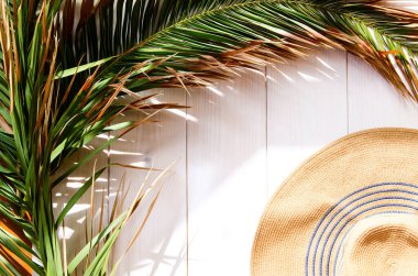 Beyaz ahşap arka planda, güneş şapkalı tropik palmiye yaprağı. Tatil ya da yaz tatili kavramı.