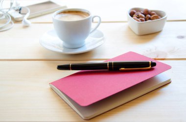 Yaratıcı kahvaltı. Bir fincan kahve, ahşap zemin üzerinde kalem ve cep telefonu olan kırmızı not defteri. Yazma kavramı. 