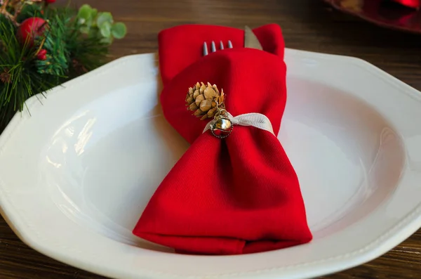 关闭餐巾环与圆锥和铃铛在白盘上 喜庆晚餐的圣诞装饰很精致 红色餐巾 带有刀叉 背景粗俗 复制空间 — 图库照片