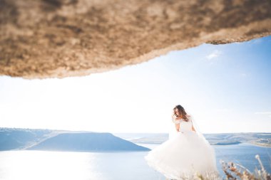 Güzel bayan, gelin gün batımında deniz kenarında bir gelinlik içinde poz veriyor.