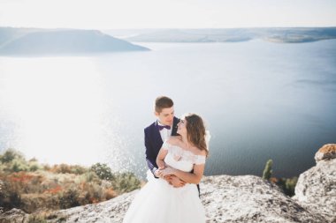 Şık, şık, mutlu bir düğün çifti, gelin, deniz ve gökyüzünün arka planında muhteşem bir damat.