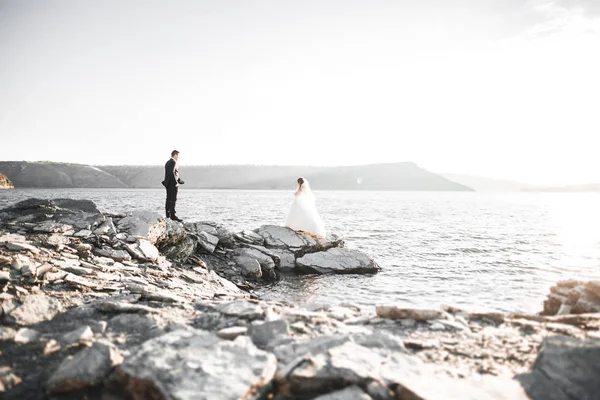 Boda pareja besándose y abrazándose en rocas cerca de mar azul — Foto de Stock