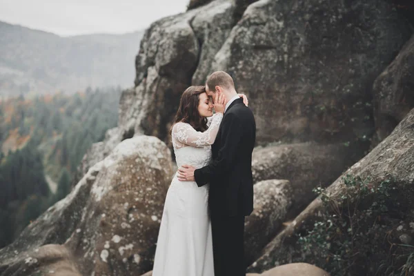 Bruiloft koppel in liefde kussen en knuffelen in de buurt van rotsen op prachtig landschap — Stockfoto