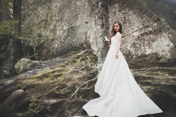Mooie bruid met een boeket poseren in bos met rotsen. Buitenshuis — Stockfoto