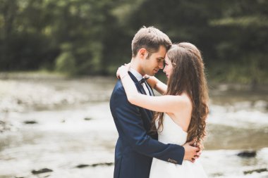 Şık şık mutlu esmer gelin ve dağlarda güzel bir nehir arka plan üzerinde muhteşem damat