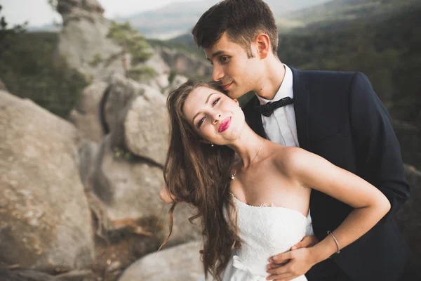 Birbirlerine aşık düğün çifti güzel manzarada kayaların yanında öpüşüyor ve sarılıyorlar. — Stok fotoğraf