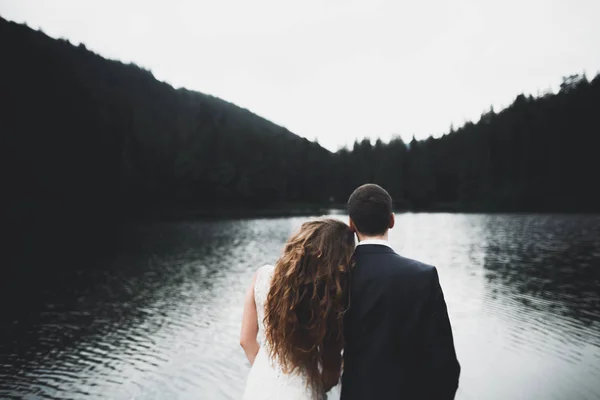 Mladý novomanželský pár, nevěsta a ženich líbání, objímání na dokonalém výhledu na hory, modrá obloha — Stock fotografie