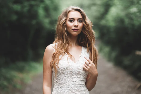 Bella sposa in elegante vestito bianco che tiene bouquet in posa nel parco — Foto Stock