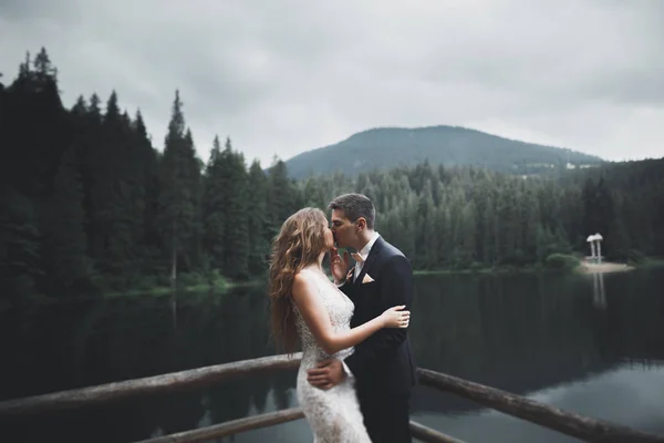 Joven pareja recién casada, novia y novio besándose, abrazándose a la vista perfecta de las montañas, cielo azul —  Fotos de Stock