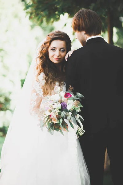 Couple élégant de jeunes mariés heureux marchant dans le parc le jour de leur mariage avec bouquet — Photo