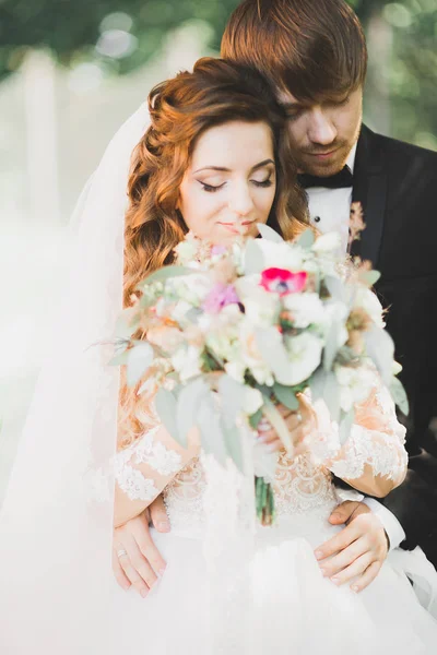 Elegante coppia di sposi felici che passeggiano nel parco il giorno del loro matrimonio con bouquet — Foto Stock