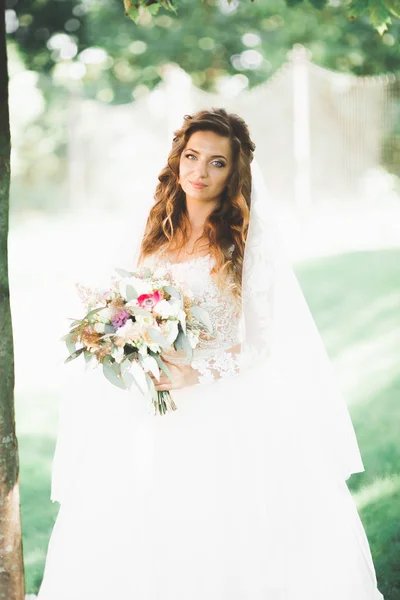 Bella sposa in elegante vestito bianco che tiene bouquet in posa nel parco — Foto Stock