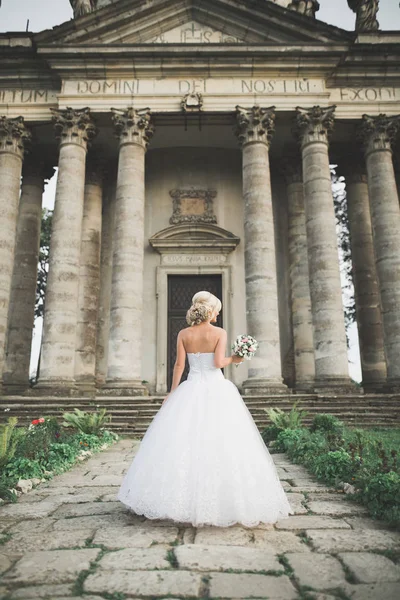 Элегантная невеста с идеальным свадебным платьем и букетом позирует возле старого замка — стоковое фото