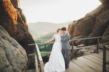 Yeni evli çift, gelin ve damat öpüşüyor, mükemmel dağ manzarasında sarılıyorlar, mavi gökyüzü