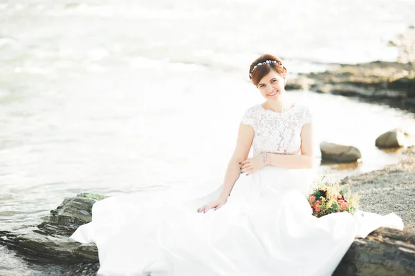 Splendida bella sposa sorride mentre posa sul fiume con bouquet — Foto Stock