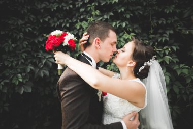 Romantik, peri masalı, mutlu yeni evli çift parkta sarılıp öpüşüyor, arka planda ağaçlar...