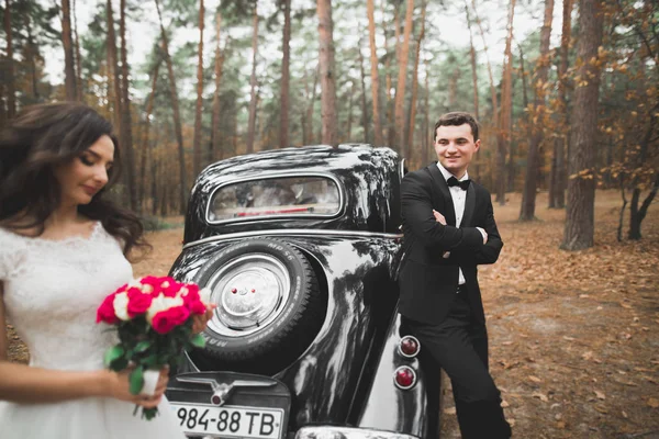 Stijlvolle bruidspaar, bruid, bruidegom zoenen en knuffelen in de buurt van retro auto in de herfst — Stockfoto