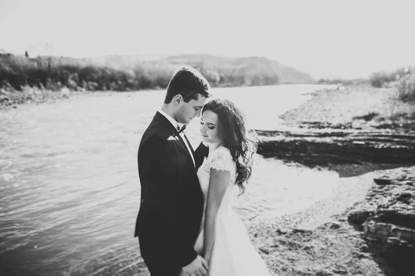 Feliz pareja recién casada posando y sonriendo en vestido de novia y traje al aire libre, blanco y negro — Foto de Stock