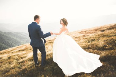 Yeni evli çift, gelin ve damat öpüşüyor, mükemmel dağ manzarasında sarılıyorlar, mavi gökyüzü