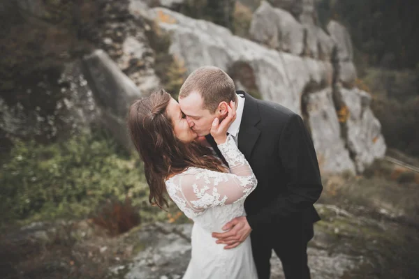 Свадебная пара влюблённая целуется и обнимается у скал на красивом ландшафте — стоковое фото
