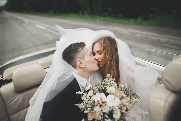 Stijlvol bruidspaar, bruid, bruidegom kussen en knuffelen op retro auto — Stockfoto