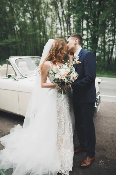 Stijlvol bruidspaar, bruid, bruidegom kussen en knuffelen op retro auto — Stockfoto