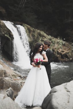 Şık şık mutlu esmer gelin ve dağlarda güzel bir nehir arka plan üzerinde muhteşem damat