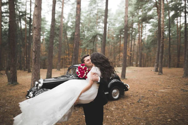 Прекрасная свадебная пара, позирующая рядом с великолепным ретро автомобилем — стоковое фото