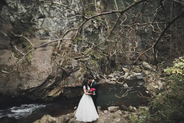 Verliebtes Hochzeitspaar küsst und umarmt sich in der Nähe von Felsen in schöner Landschaft — Stockfoto