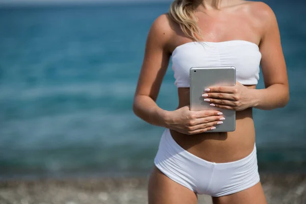 스포츠 한 벌에서 젊은 아름 다운 여자 해변에서 그녀의 태블릿을 사용 하는 — 스톡 사진