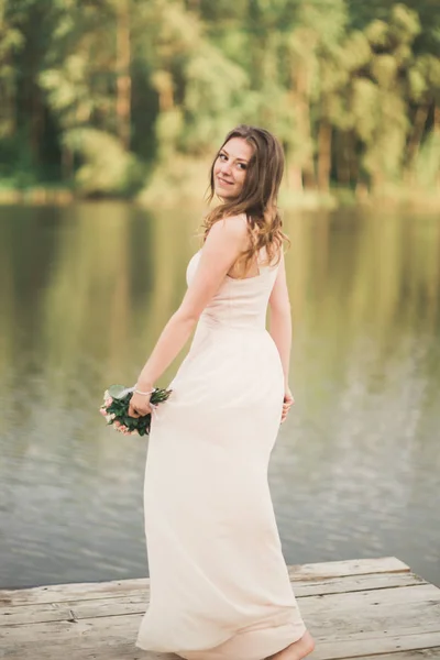 Чудова наречена в елегантній сукні тримає букет позує біля лісу і озера — стокове фото