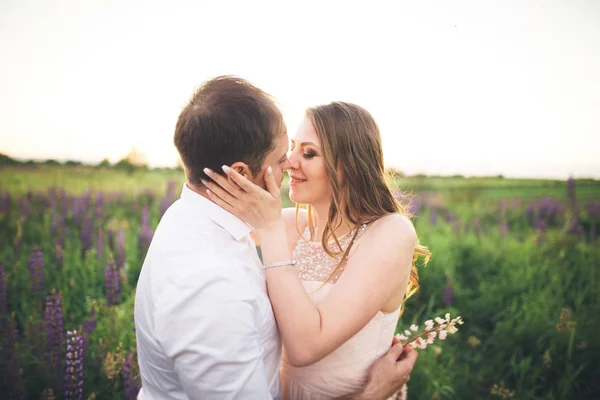 Bruid houdt bruidegoms nek terwijl hij haar in de stralen van de zonsondergang kust — Stockfoto