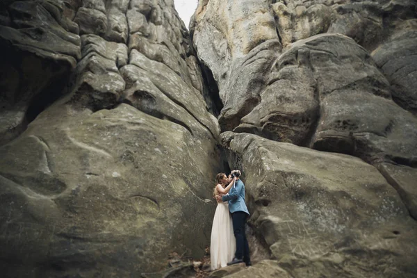 Счастливая супружеская пара целуется и обнимается у высокой скалы — стоковое фото