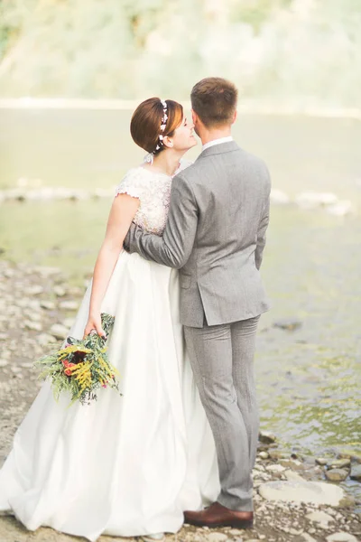 Menyasszony és a vőlegény gazdaság gyönyörű esküvői csokor. Jelentő folyó közelében — Stock Fotó