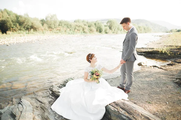 Novia y novio celebrando hermoso ramo de bodas. Posando cerca del río —  Fotos de Stock