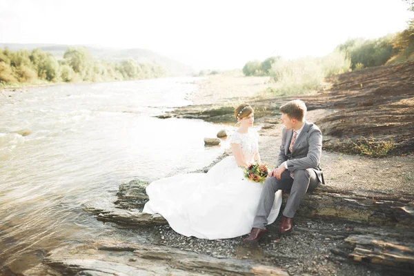 Guapo romántico novio y hermosa novia posando cerca del río en las montañas escénicas —  Fotos de Stock