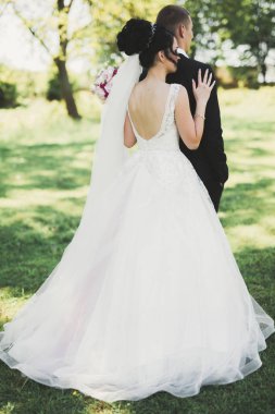 Romantik, peri masalı, mutlu yeni evli çift parkta sarılıp öpüşüyor, arka planda ağaçlar...