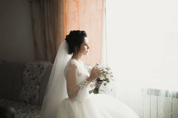 Hermosa novia con vestido de novia de moda con plumas con maquillaje de lujo deleite y peinado, estudio sesión de fotos interior — Foto de Stock