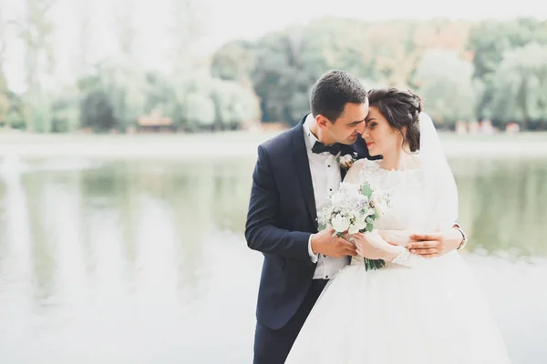 Pasangan pengantin baru yang bahagia berjalan di taman pada hari pernikahan mereka dengan karangan bunga — Stok Foto
