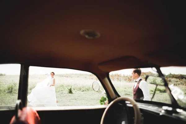 Elegante pareja de boda, novia, novio besándose y abrazándose en coche retro — Foto de Stock