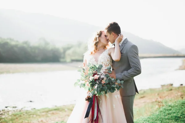 Romantis, dongeng, pasangan pengantin baru yang bahagia memeluk dan mencium di taman, pohon dan sungai di latar belakang — Stok Foto